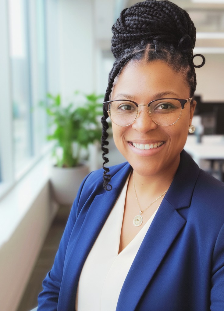 Stefanie Hodnett The Prompt Coach leaning up against the wall in the office with her arms politely folded she has a bright smile