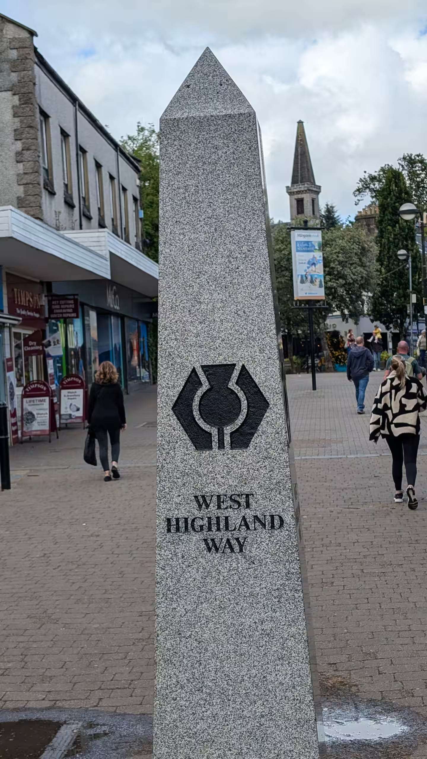 River in the middle of a road and grassy field with a rainbow in the distance at daytime